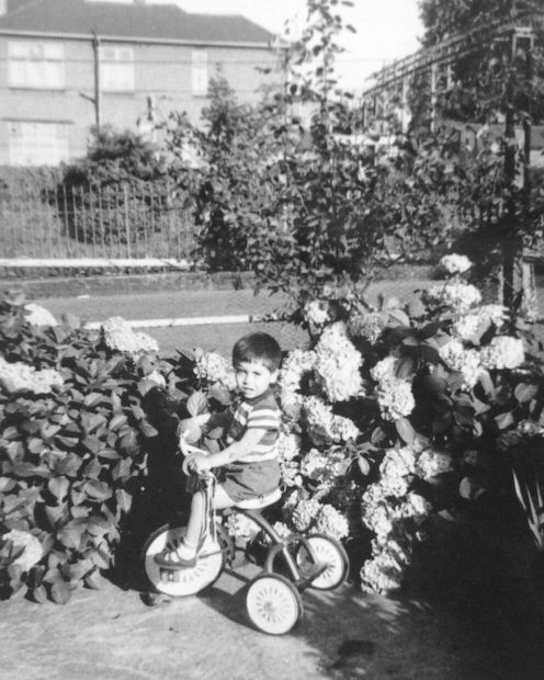 George Costa as a young boy, riding a tricycle in a garden