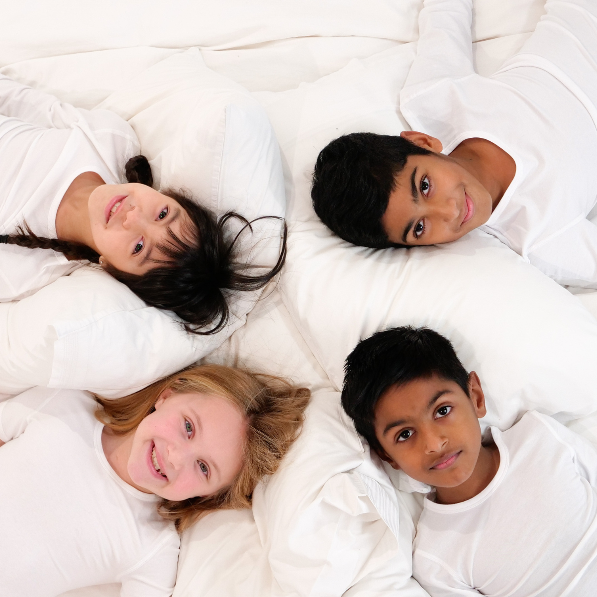 four smiley children lay down on white bed